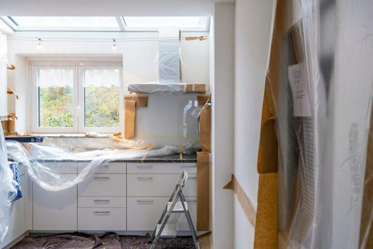 A kitchen under renovation with white cabinets covered in plastic and brown paper